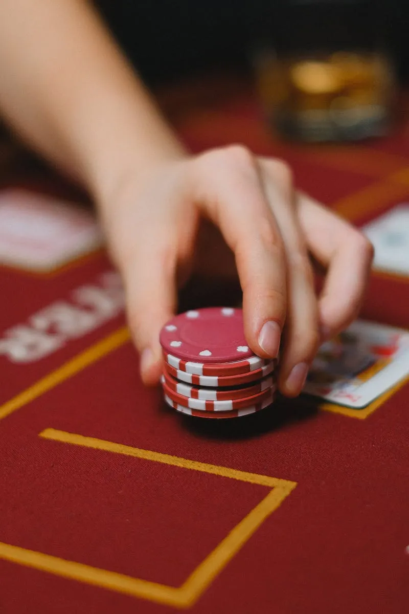 Main posée sur une pile de jetons rouges sur table de casino — chips et mise au blackjack en anglais